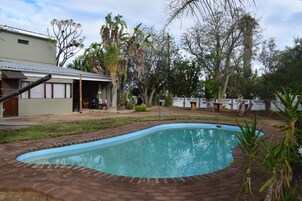 Piscina con borde de ladrillo, rodeada por un césped y árboles.