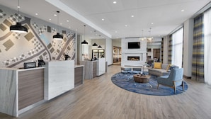 A modern hotel lobby with a reception desk, seating area, and a fireplace. - Homewood Suites by Hilton Boston Woburn (Woburn)