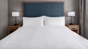 Una cama bien hecha con cabecera capitonada, dos mesitas de noche con lámparas y una mesita auxiliar de madera.