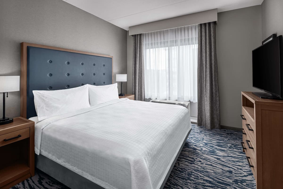 Habitación de hotel con una cama grande, televisión, escritorio con lámpara y ventana con cortinas.