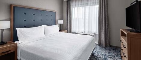 Habitación de hotel con una cama grande, televisión, escritorio con lámpara y ventana con cortinas.