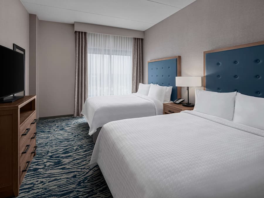 Quarto de hotel com duas camas, televisão, escrivaninha e abajur.
