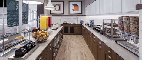 A modern kitchen with a long counter, various food dispensers, and a fruit bowl.