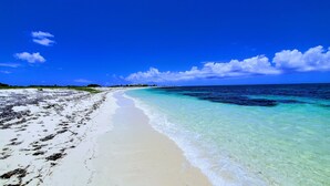 Une plage aux eaux turquoise et limpides, au sable blanc et sous un ciel dégagé.