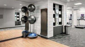 Une salle de sport équipée de matériel d’exercice, dotée d’un plancher en bois et d’un espace recouvert de moquette grise.