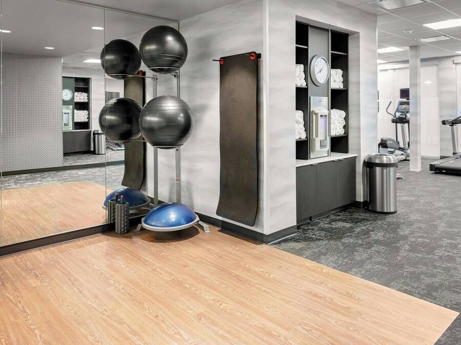 A gym with exercise equipment, a wooden floor, and a grey carpeted area.