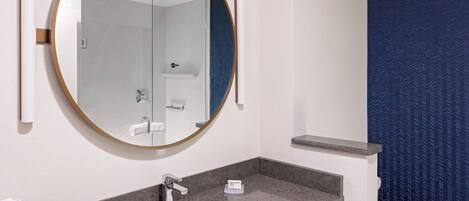 A bathroom with a round mirror, a sink, a towel dispenser, and a toilet.