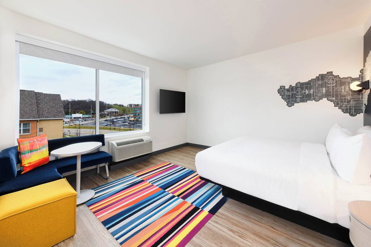 A hotel room with a large bed, a sofa, a small table, and a colorful striped rug.