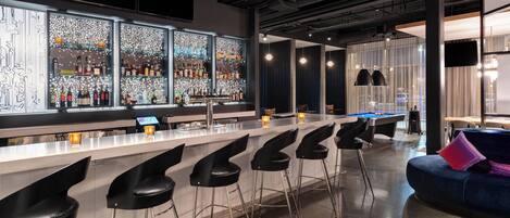 A modern bar area with a long counter, black bar stools, and a pool table.
