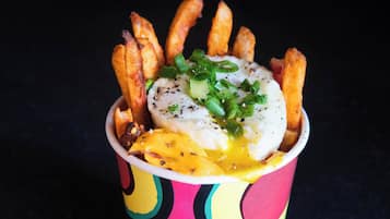 Un plato de comida con papas fritas, un huevo escalfado y queso derretido.