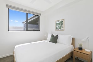 Une chambre à coucher avec un grand lit, une fenêtre, une table de chevet avec une lampe et un tableau encadré au mur.