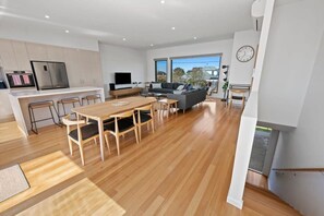 A modern kitchen with a dining area, a living room with a sofa and TV, and a large window.