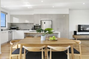 A modern kitchen with white cabinets, a dining table with chairs, a potted plant, and a bowl of apples.
