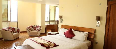 A hotel room with a large bed, two armchairs, a desk, and a window.