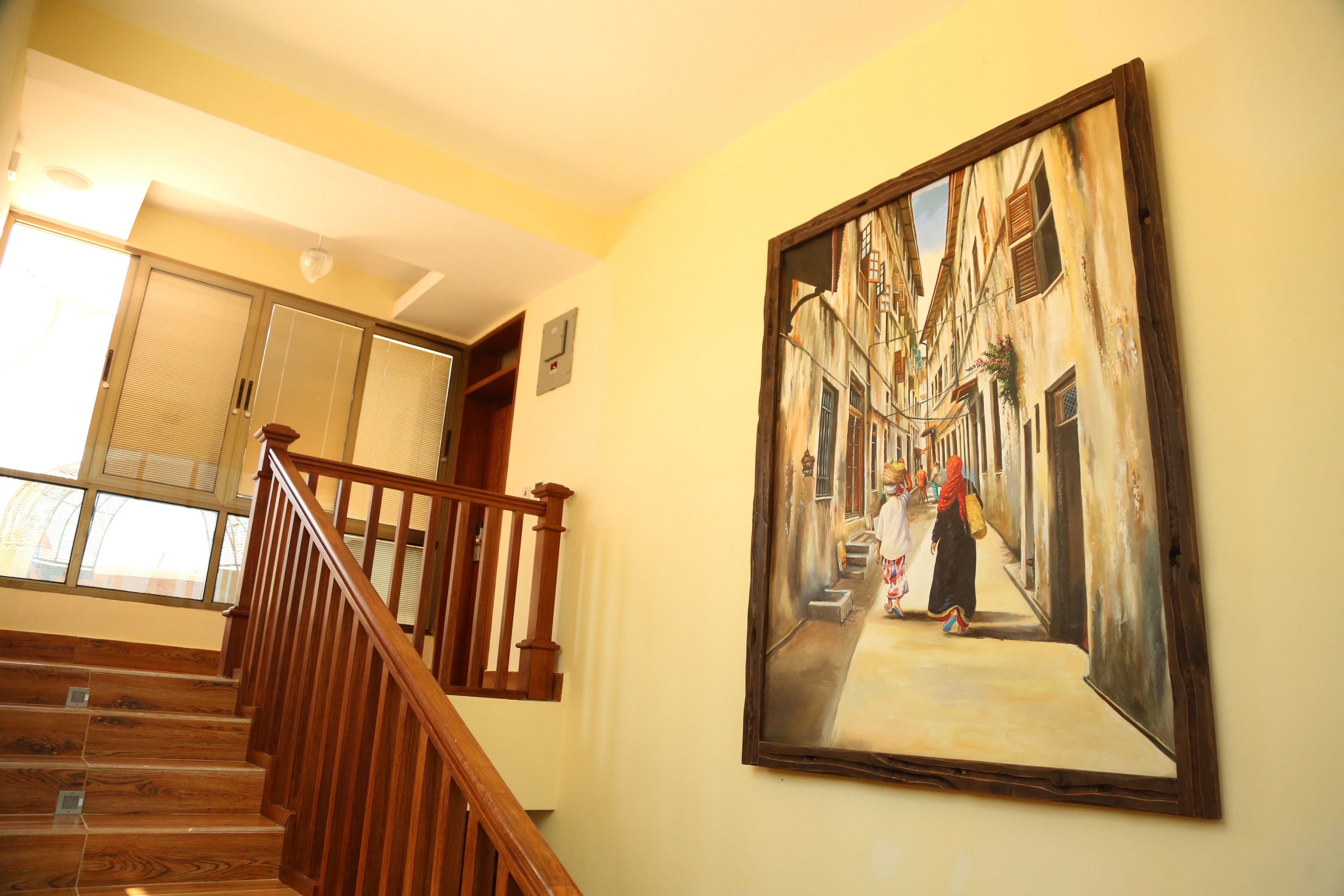 Een trap met houten leuningen die leidt naar een kamer met een groot schilderij van een straatbeeld.