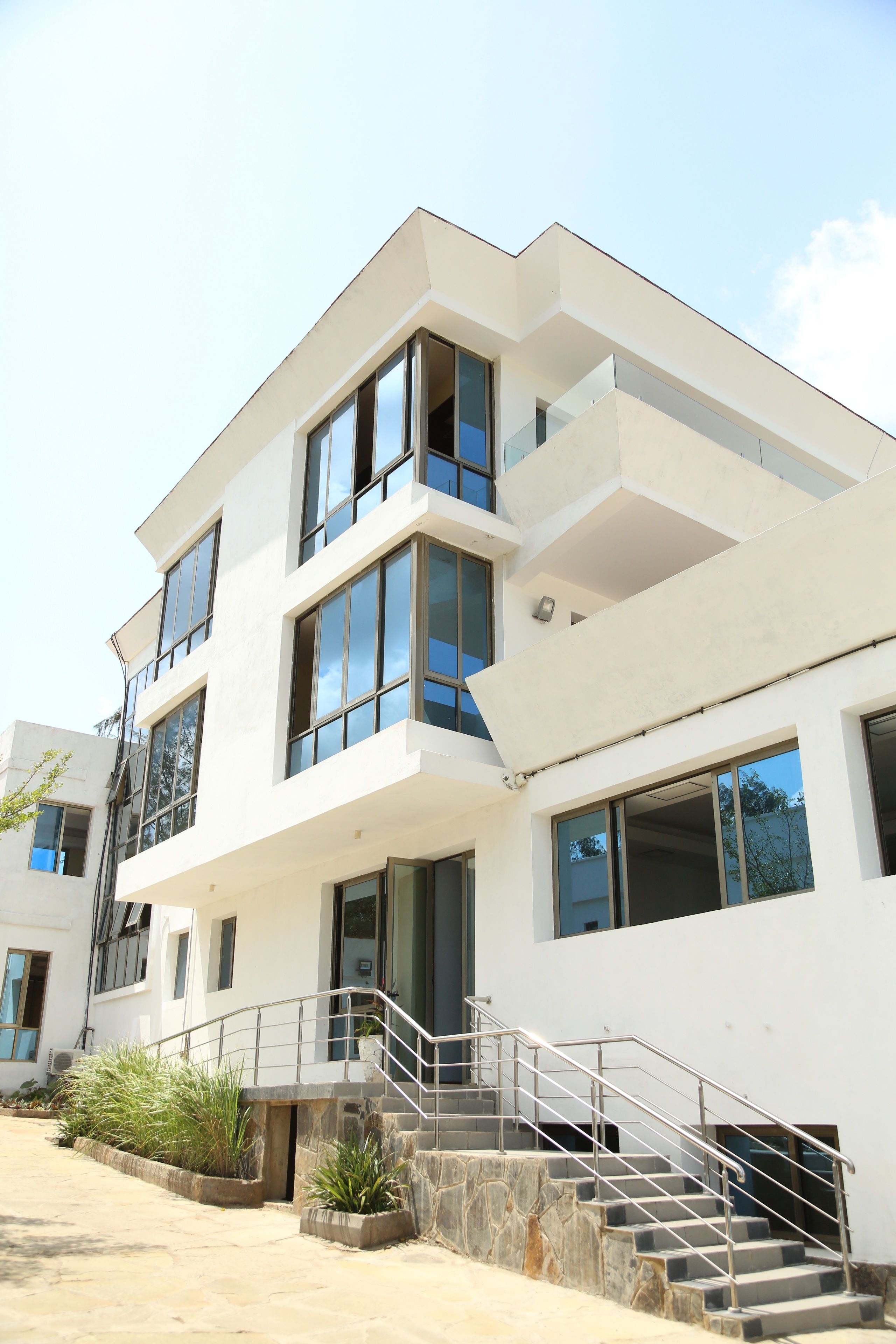 A modern multi-story building with large windows, a staircase with metal railings, and a flat roof.