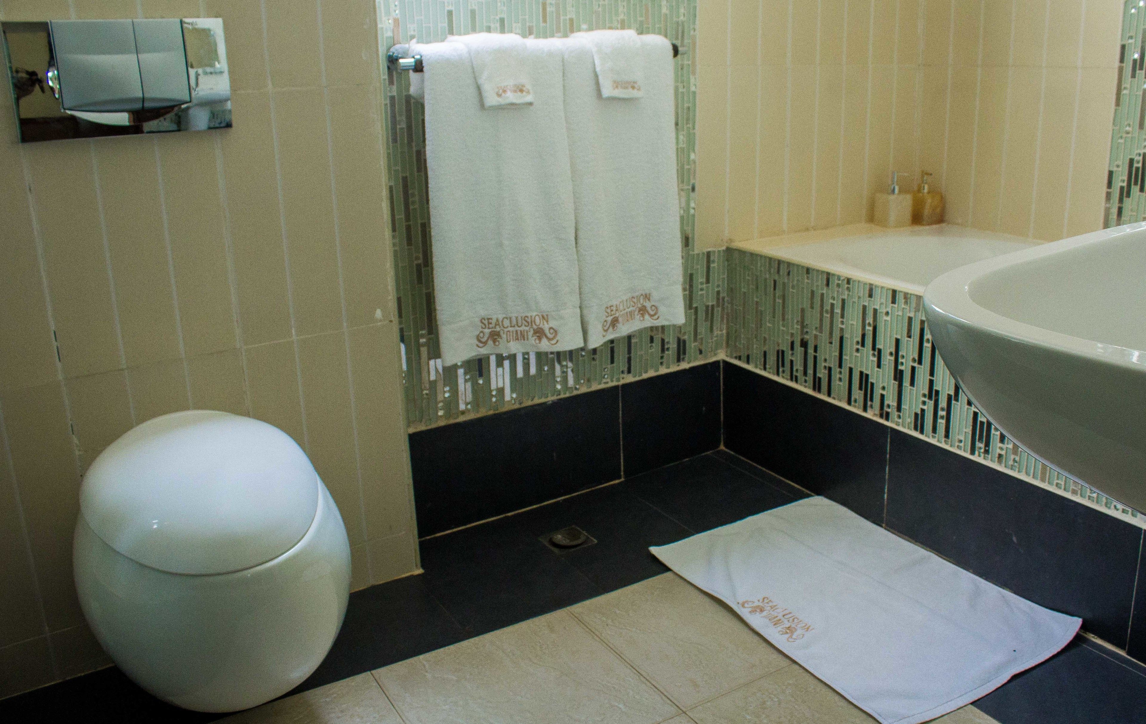 Un baño con inodoro, lavabo y bañera. Hay dos toallas blancas colgadas en la pared.