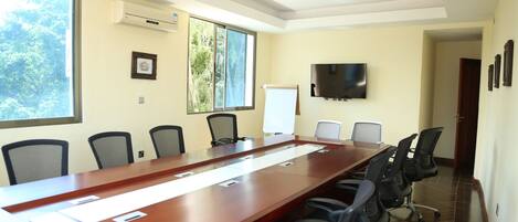 A conference room with a long table, chairs, a whiteboard, and a TV on the wall.