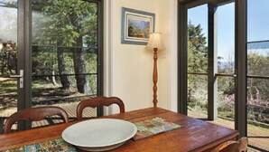 A dining area with a wooden table, chairs, and a view of trees through large windows. - Narrow Neck Views - Spacious Mountains Home with Stunning Views! (Katoomba)