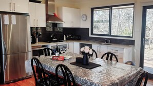A modern kitchen with stainless steel appliances, a dining table with chairs, and a large window offering a view of trees. - Narrow Neck Views - Spacious Mountains Home with Stunning Views! (Katoomba)