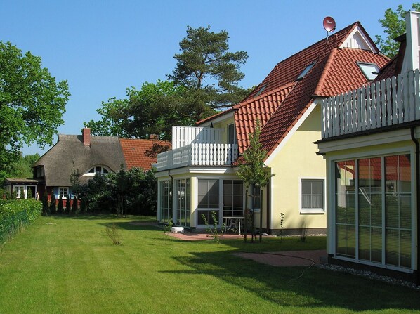 Ett bostadsområde med ett hus som har ett rött tegeltak, ett vitt staket och en välskött gräsmatta.