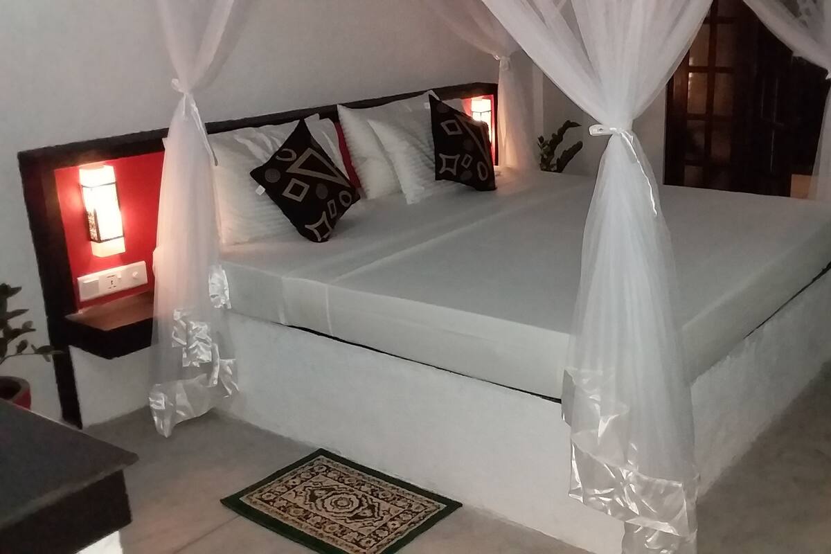 Una cama bien hecha con dosel, una mesita de noche con lámpara y una alfombra estampada en el suelo.