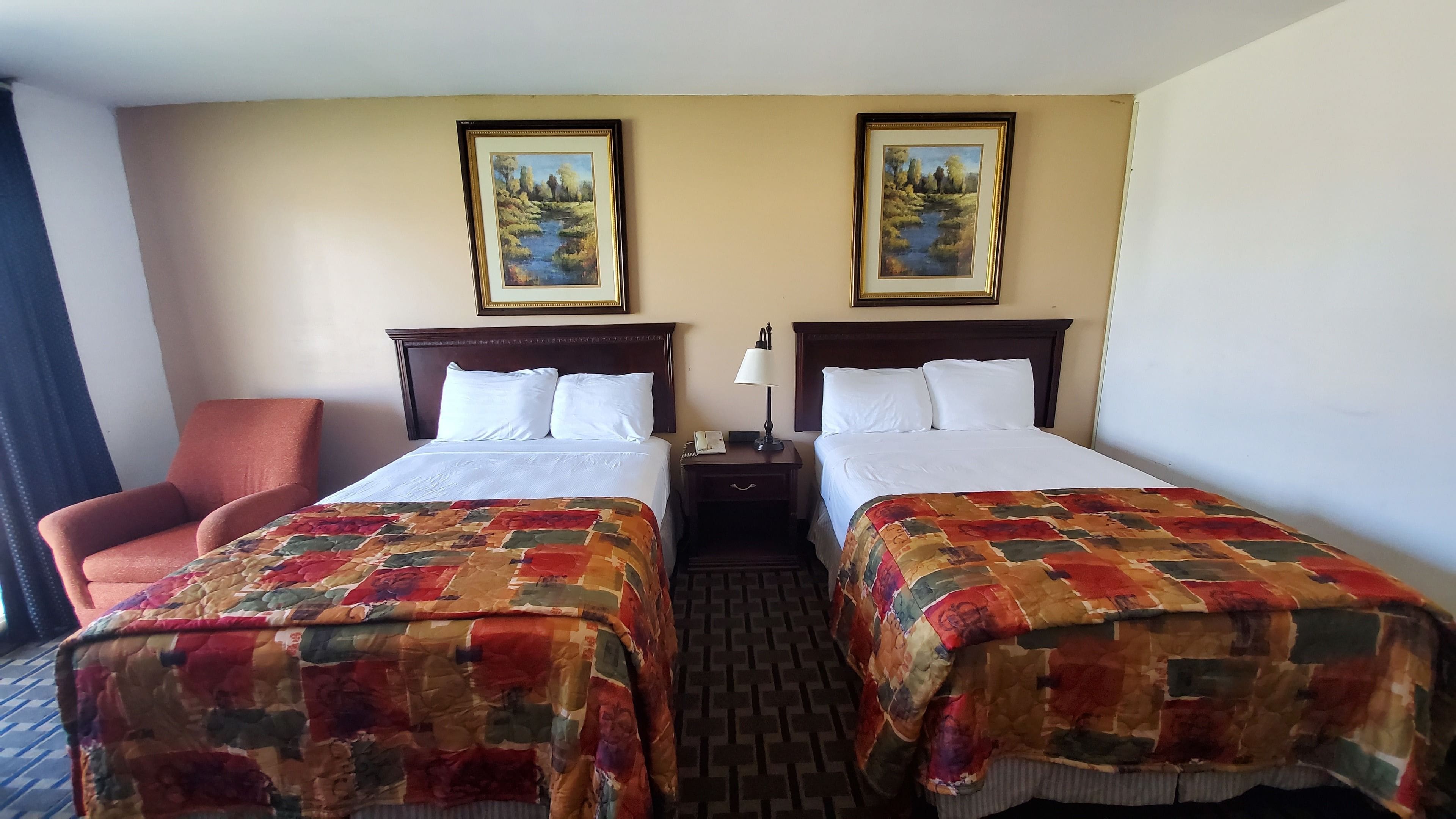 A hotel room with two beds, a chair, and two paintings on the wall.