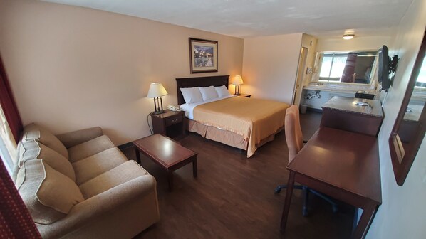 Habitación de hotel con cama, sofá, escritorio y una mesita. Hay un cuadro en la pared y una ventana con vistas.
