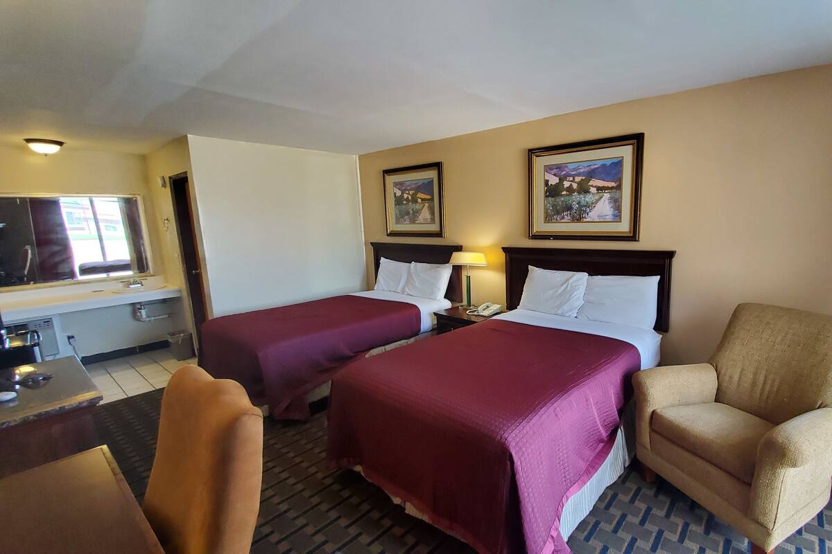 Habitación de hotel con dos camas, un escritorio con teléfono, una silla y dos cuadros en la pared.