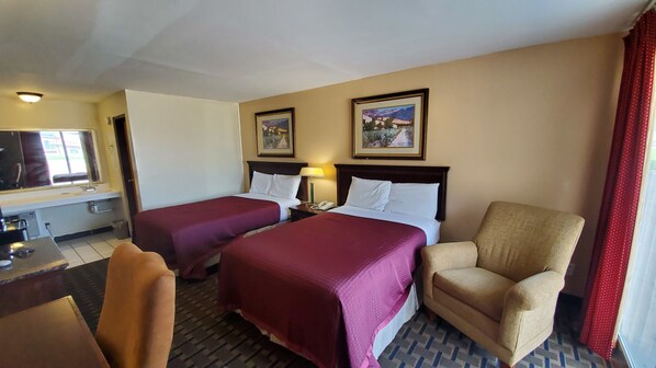 A hotel room with two beds, a desk with a telephone, a chair, and two framed pictures on the wall.