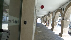 A covered walkway with stone arches, a red emergency symbol, and a sign reading "San Nicolás". - Casa San Nicolás (Portomarin)