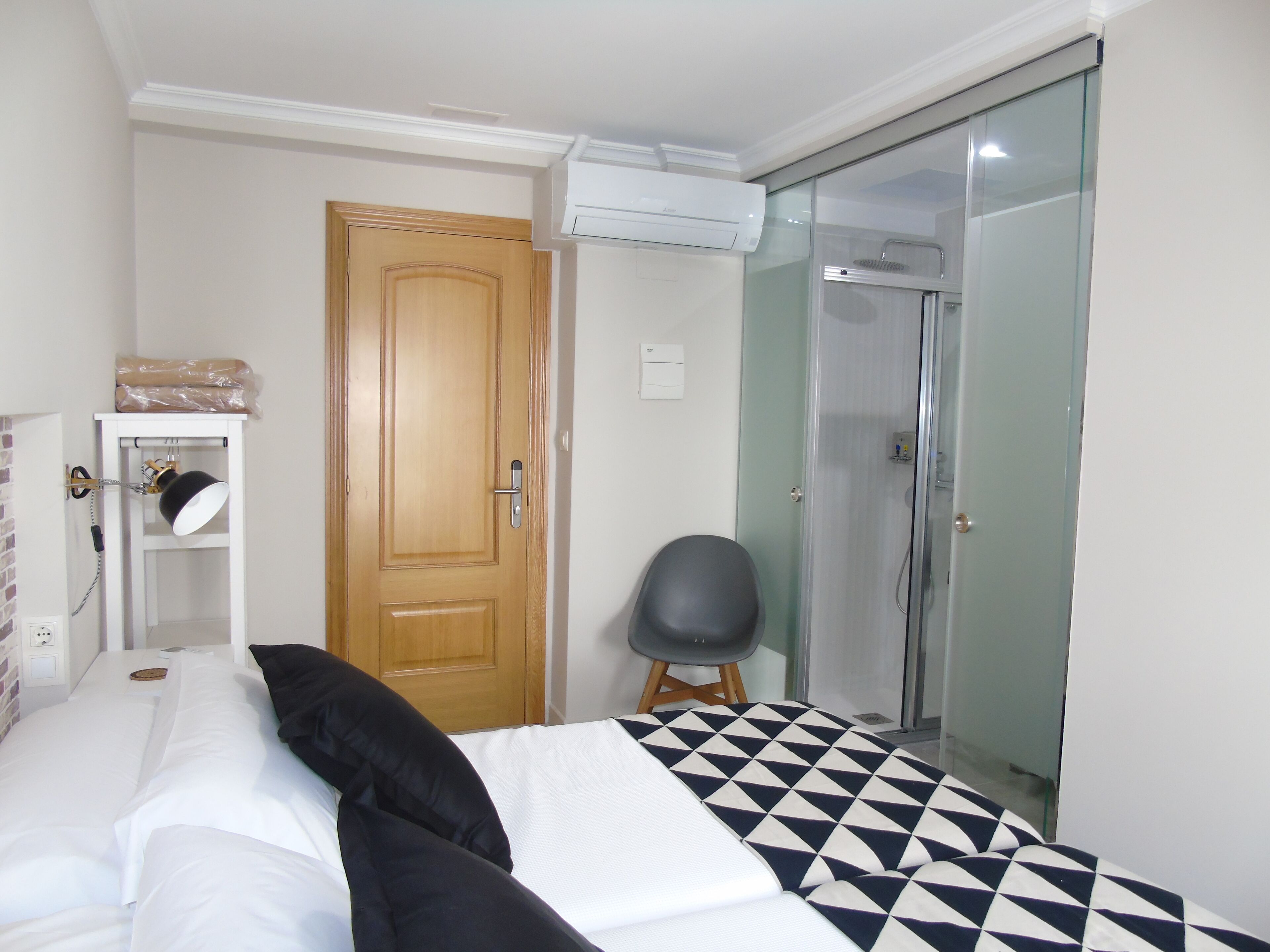 Une chambre avec un lit, une porte en bois, un appareil de climatisation, une douche et une chaise.