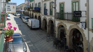 A street with parked cars, a café-bar, and a building with a sign for 'Rosalia de Castro'. - Casa San Nicolás (Portomarin)
