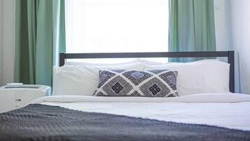 Een opgemaakt bed met een gestreept kussen, een nachtkastje en een raam met gordijnen.
