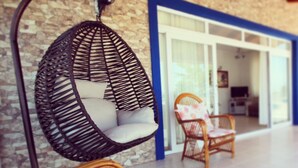 A wicker chair with a cushion and a hanging chair with a cushion against a stone wall. - Kumsal Suit (Marmara)