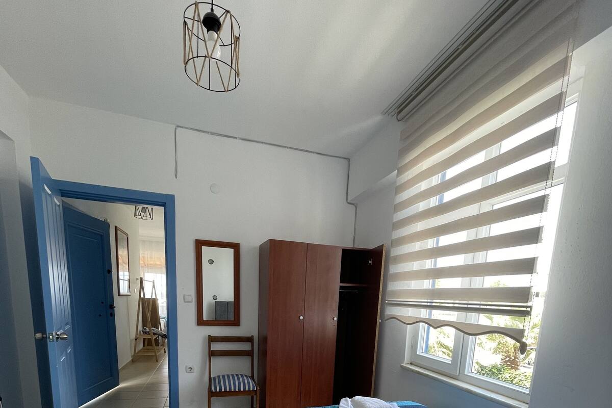 A hotel room with two beds, a wardrobe, a mirror, a chair, and a window with blinds.