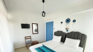 A bedroom with a bed, a chair, a small table, a TV, and a blue door. - Kumsal Suit (Marmara)