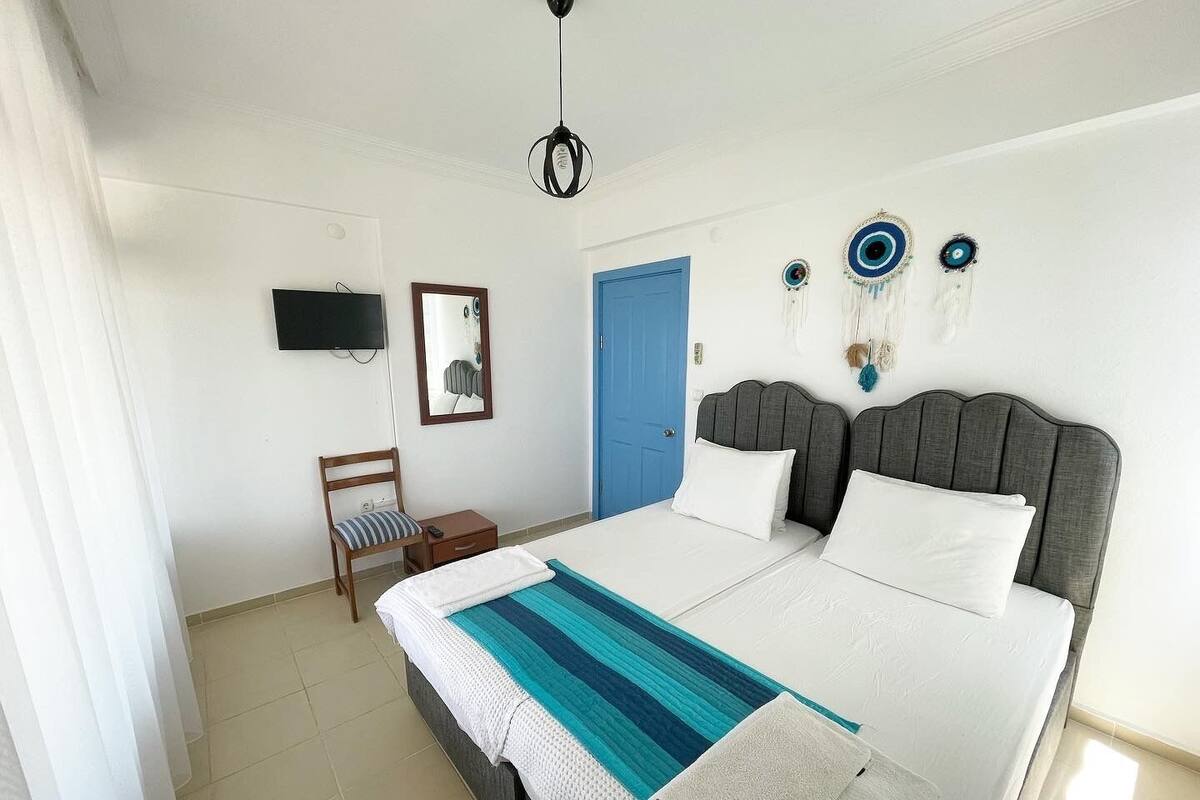 A bedroom with a bed, a chair, a small table, a TV, and a blue door.