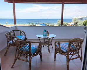 Un balcón con mobiliario de mimbre, una mesa de vidrio y vista al mar.