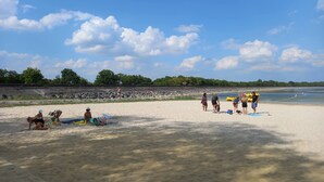 Een zanderig strand met mensen en kajaks, een rotsachtige kustlijn en bomen op de achtergrond.