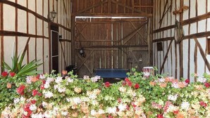 Een rustiek interieur van een schuur met een houten plafond, een zwarte bank en een verscheidenheid aan kleurrijke bloemen op de voorgrond.