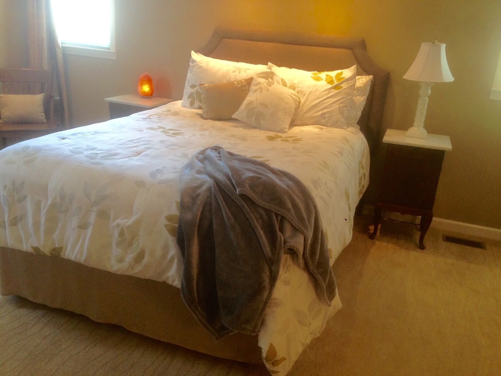 Un lit bien fait, recouvert d’une couvre-lit à motifs floraux et agrémenté de plusieurs coussins, une lampe de chevet et une table de chevet avec une lampe.