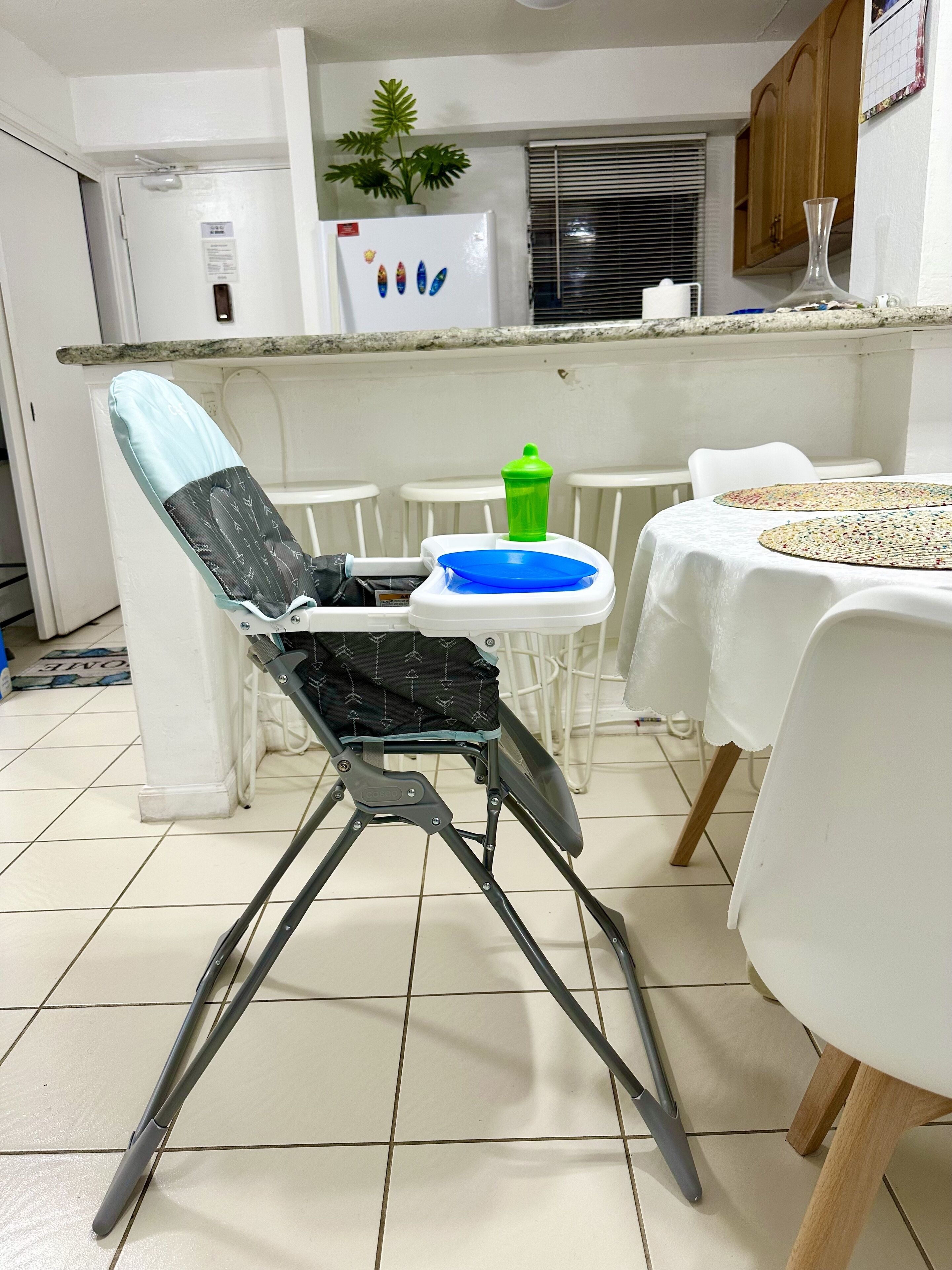 Een keuken met een hoog aanrecht, een koelkast met magneetjes, een potplant en een eettafel met stoelen.