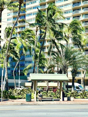Un hotel de varios pisos con balcones, palmeras y una zona de estar cubierta.