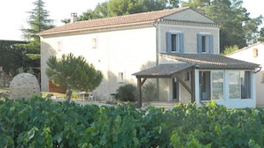 A two-story house with a tiled roof, a covered porch, and a stone wall.