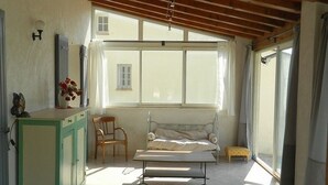 A room with a wooden ceiling, a bed, a small table, a cabinet, and a window with curtains.