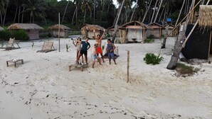 Ein sandiger Strand mit strohgedeckten Hütten und einem kleinen Holztisch mit Flaschen.