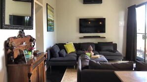 A modern living room with a sofa set, a wooden cabinet, a flat-screen TV, and a large window. - Jardin Tiny House (Beechmont)