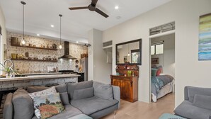 A modern living room with a grey sofa, a coffee table, and a dining area with a brick wall and pendant lights. - Jardin Tiny House (Beechmont)
