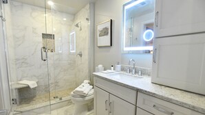 Un baño moderno con ducha de vidrio, inodoro y tocador con espejo.